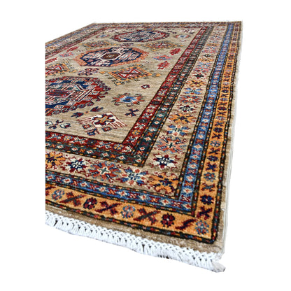 Angled view of Afghan Super Kazak rug showing navy and rust medallions, ochre borders and pale fringe
