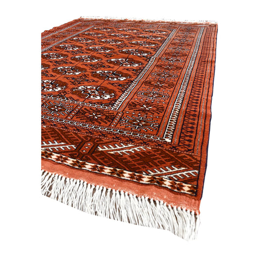 Angled view of Afghan Turkmen Tekke wool rug showing its gul field, geometric borders and ivory fringe