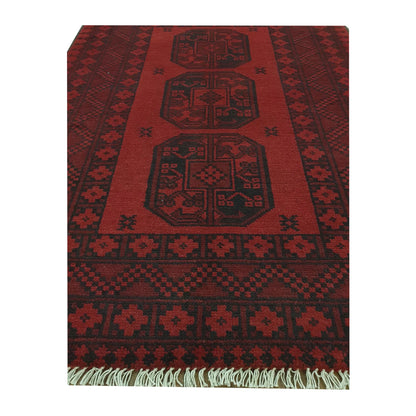 Angled full view of Afghan Turkoman wool rug showing red field, dark border and fringe detail