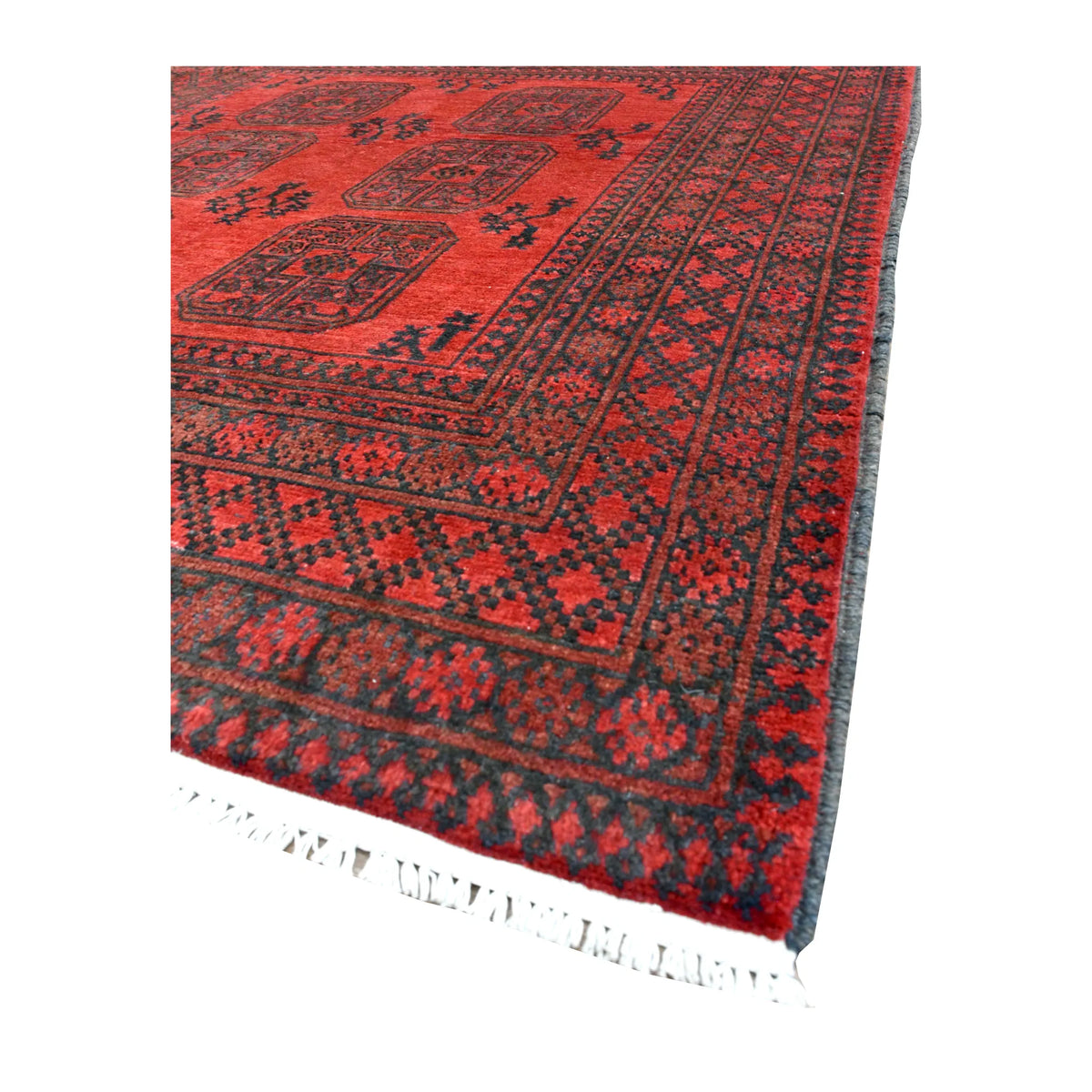 Angled view of Afghan Turkoman rug showing its rich red pile, dark gul motifs, densely patterned borders and ivory fringe