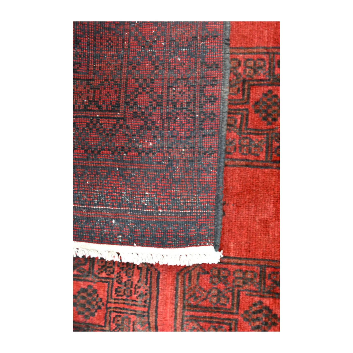 Folded-corner detail of Afghan Turkoman rug showing the reverse weave, red patterned front and ivory fringe