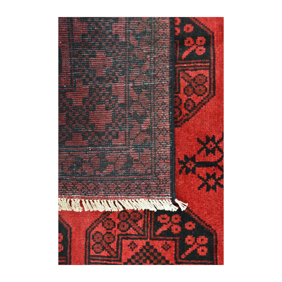 Folded-corner detail of Afghan Turkoman rug showing the reverse weave, red patterned front and pale fringe