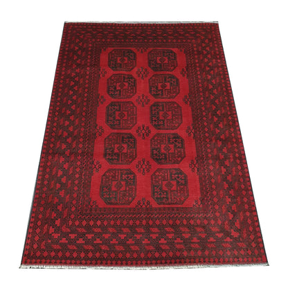 Angled view of Afghan Turkoman hand-knotted wool rug with red field, dark geometric border and ivory fringe, 240 x 163 cm