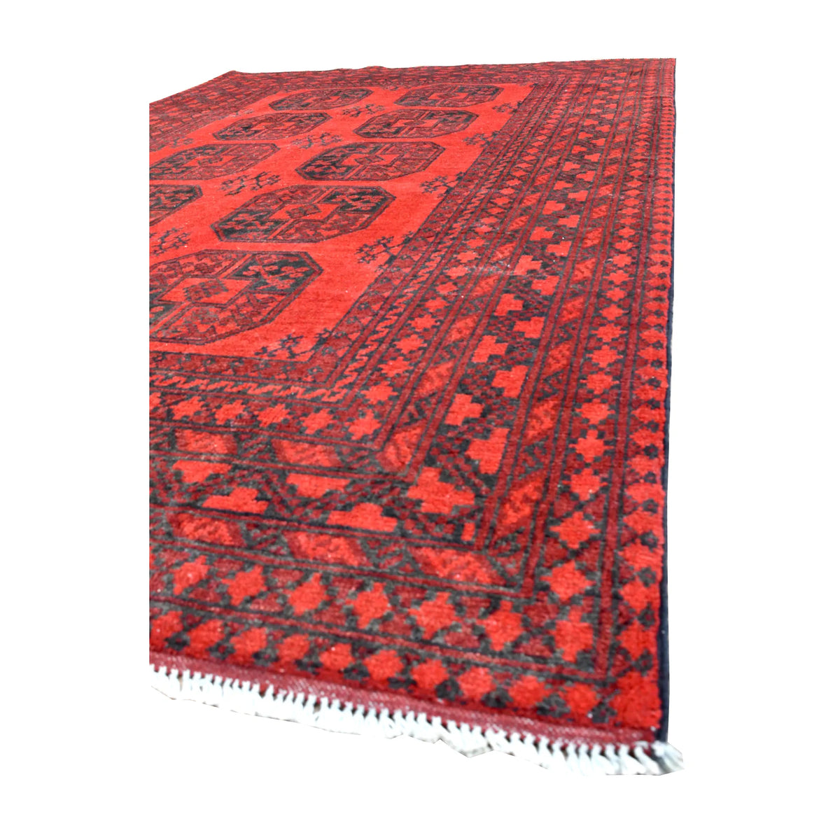 Angled view of Afghan Turkoman rug showing its red gul field, densely patterned dark border and white fringe