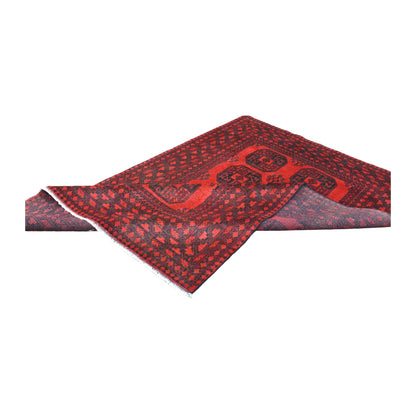 Folded view of Afghan Turkoman wool rug showing its red gul field, geometric border and turned-back corner