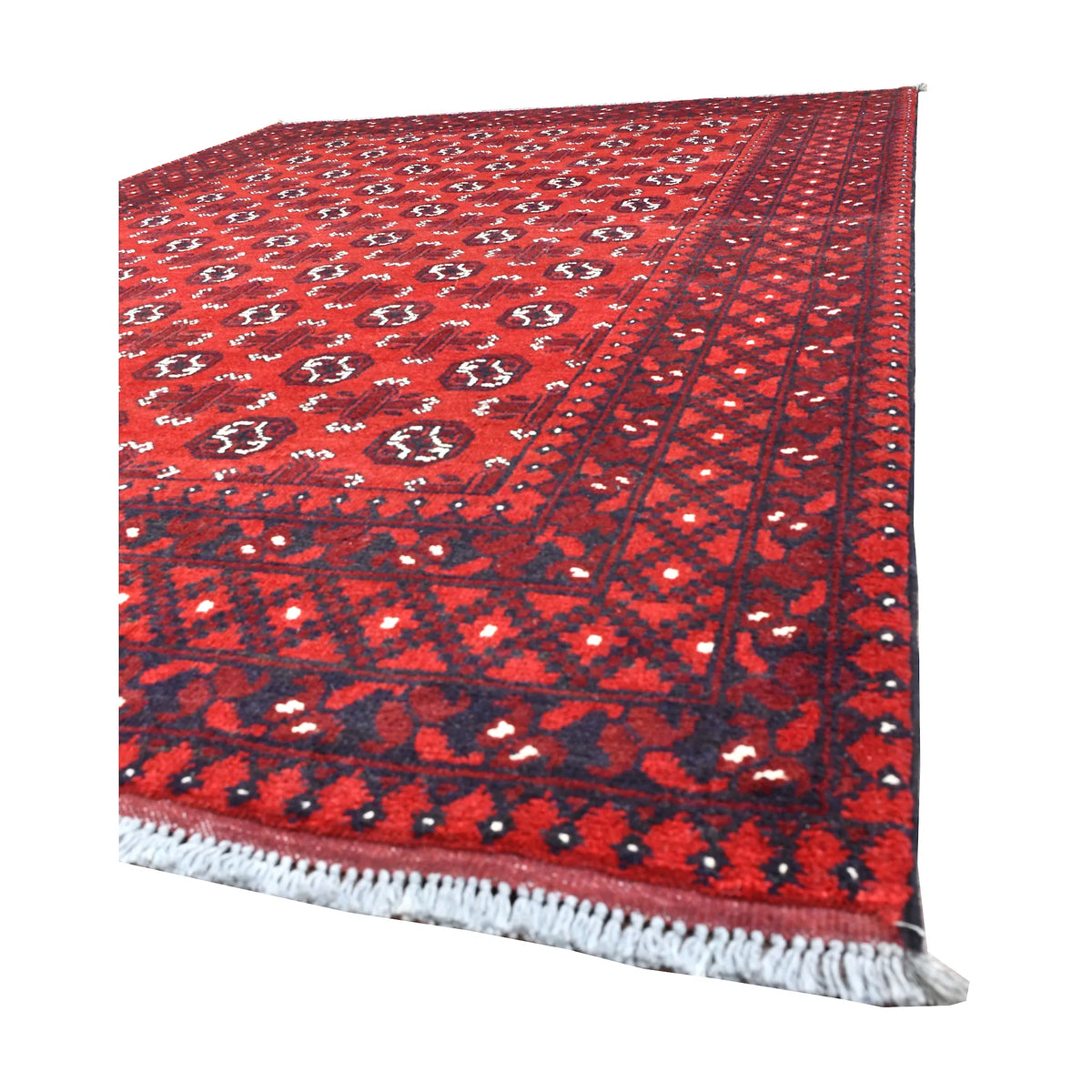 Angled view of Afghan Turkoman wool rug showing its red gul-patterned field, dark geometric border and white fringe