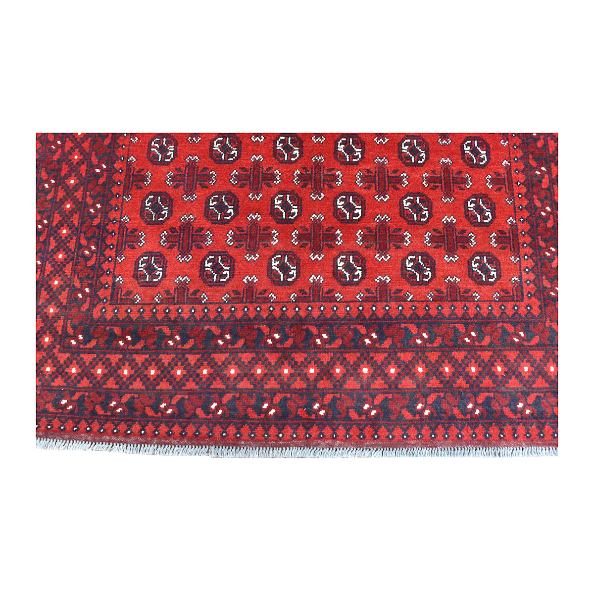 End-border detail of Afghan Turkoman rug showing red field motifs above a dark diamond lattice and white fringe