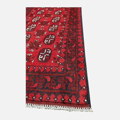 Angled corner and fringe view of Afghan Turkoman hand-knotted wool runner rug showing red field, geometric border and light fringe