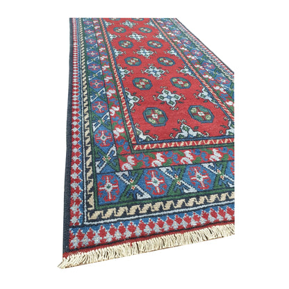 Angled full view of Afghan Turkoman wool runner rug showing red field, fringe and traditional geometric border