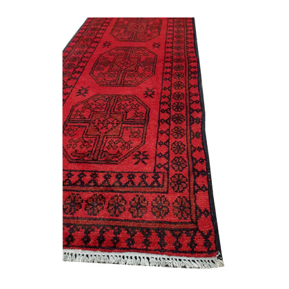 Angled corner and fringe view of Afghan Turkoman wool runner rug showing red field, dark geometric border and light fringe