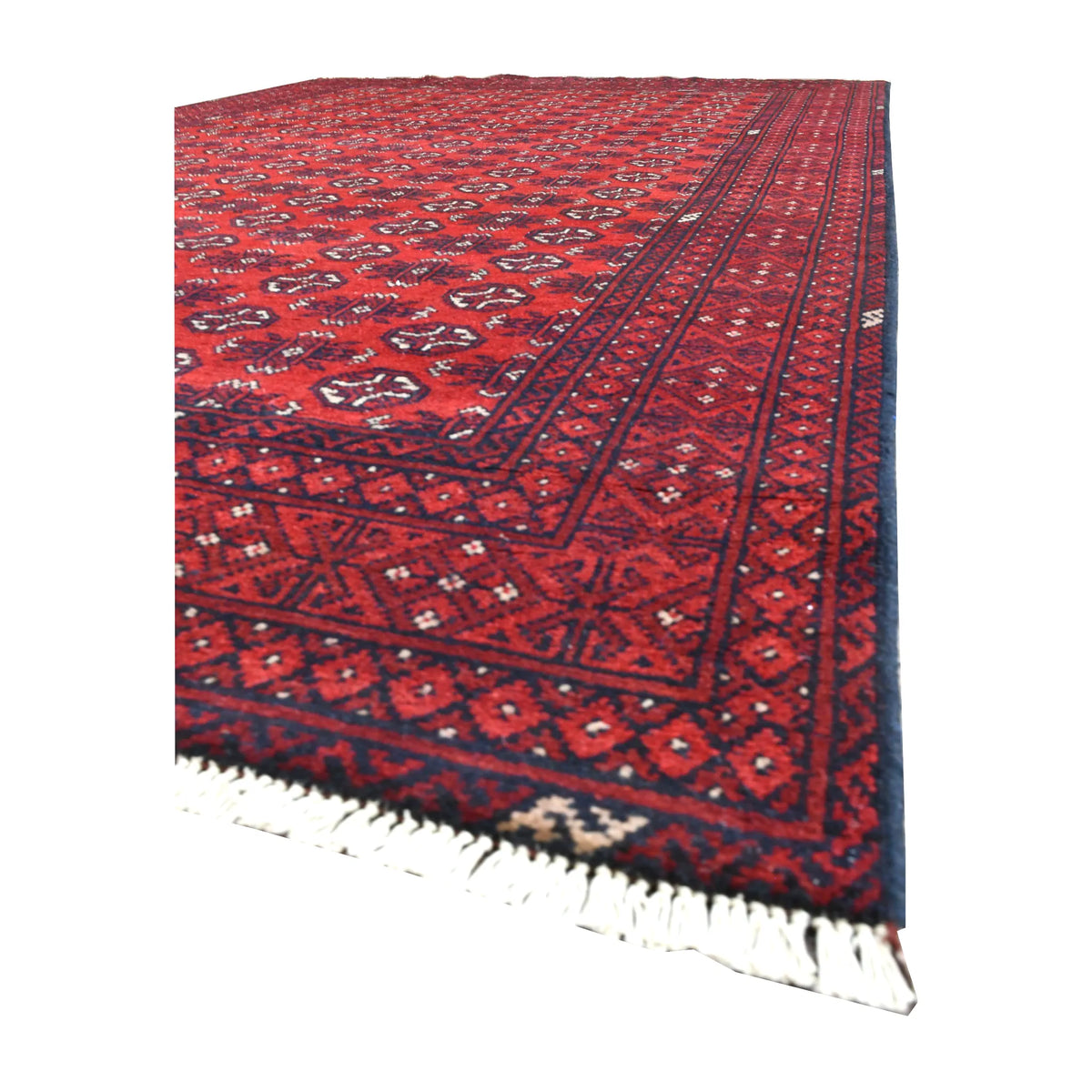 Angled view along the Afghan Turkoman rug showing its red gul field, layered dark borders and pale fringe
