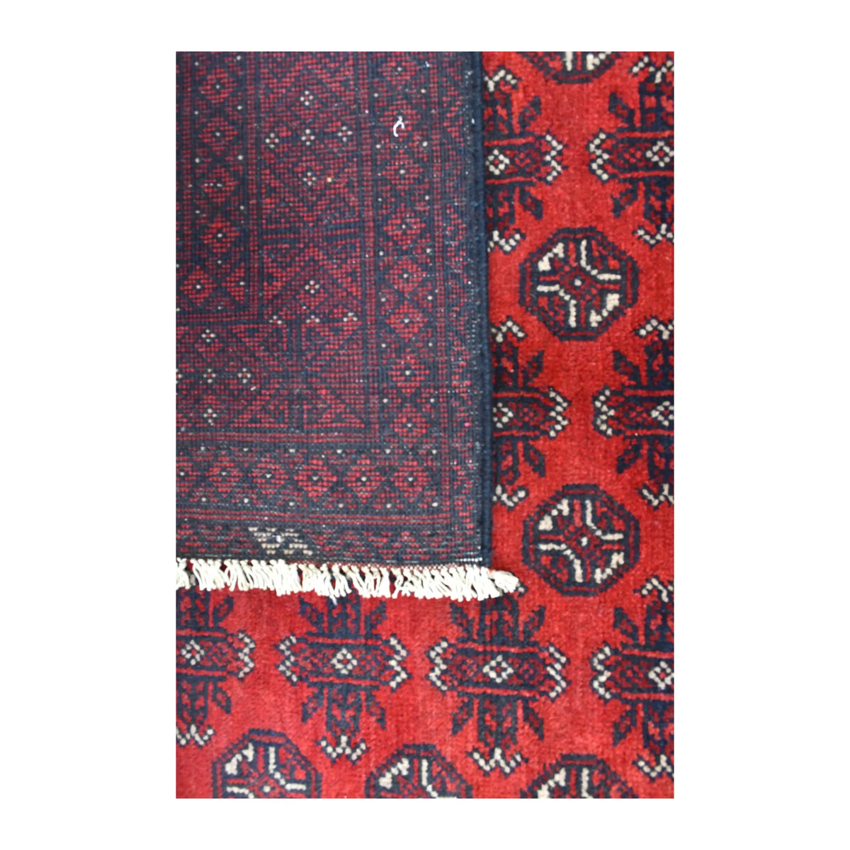 Close-up of a folded corner showing the patterned reverse beside the Afghan Turkoman rug’s red field and pale fringe