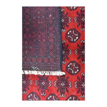 Close-up of a folded corner showing the patterned reverse beside the Afghan Turkoman rug’s red field and pale fringe