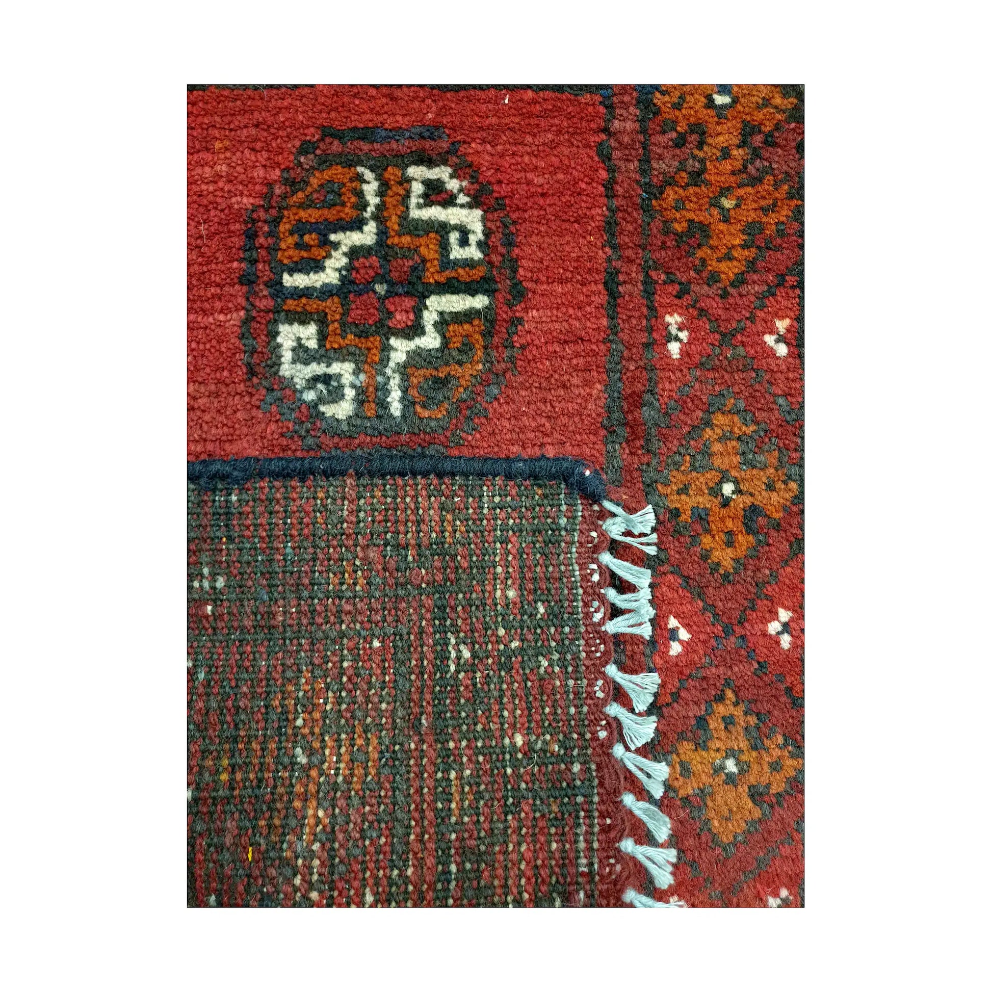 Folded corner detail of Afghan Turkoman red wool rug showing the back, fringe and red front pattern