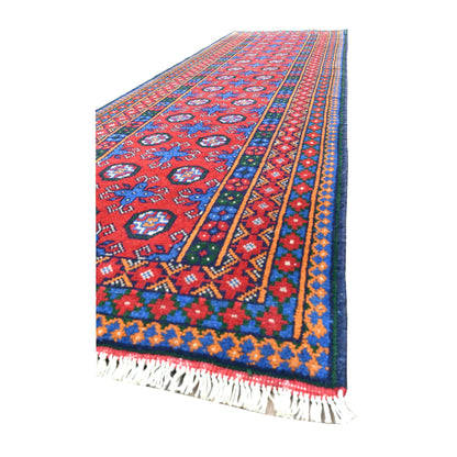 Angled view of Afghan Turkoman runner showing its red geometric field, colourful layered borders and pale fringe