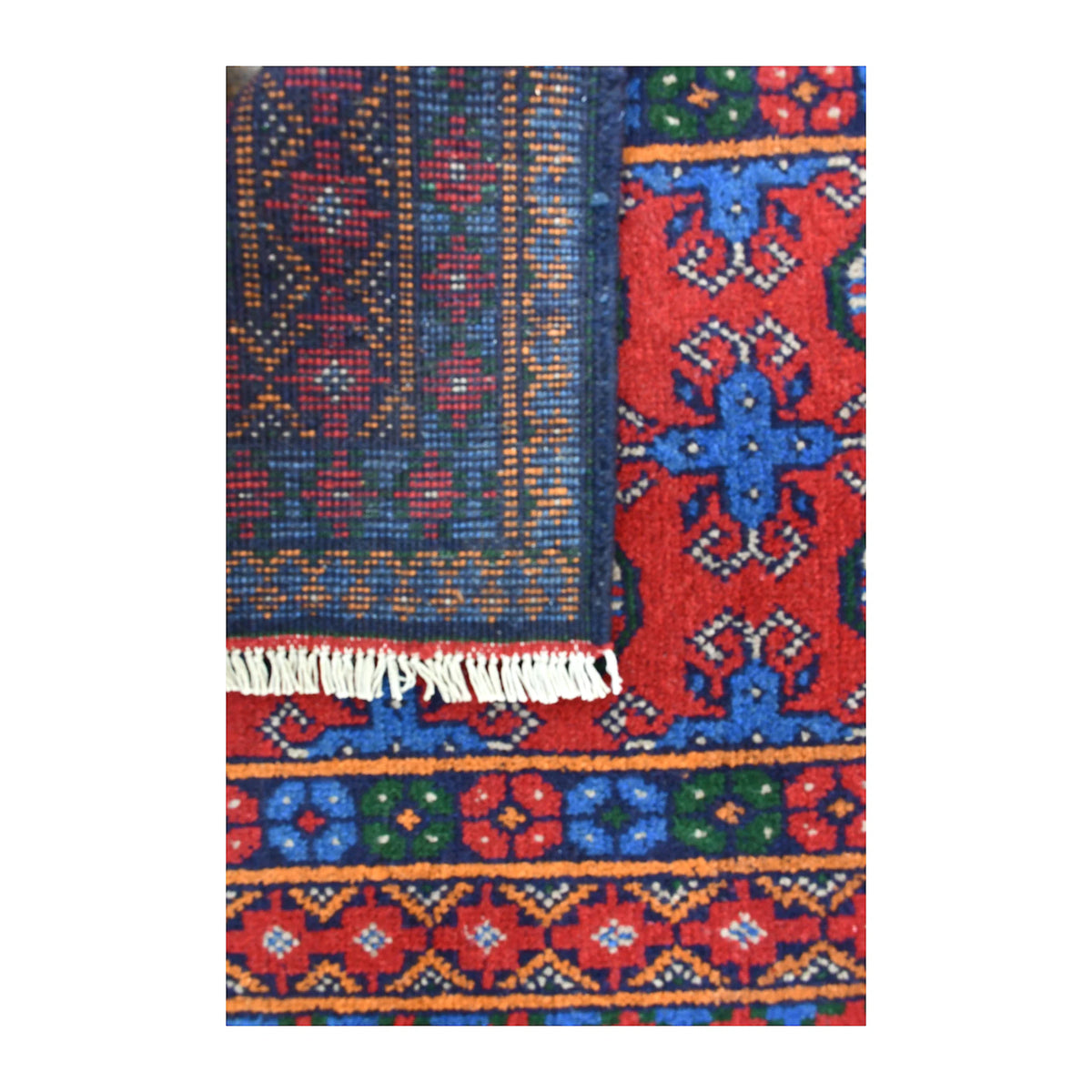 Folded-corner detail of Afghan Turkoman runner showing the patterned reverse beside its red front, blue border and pale fringe
