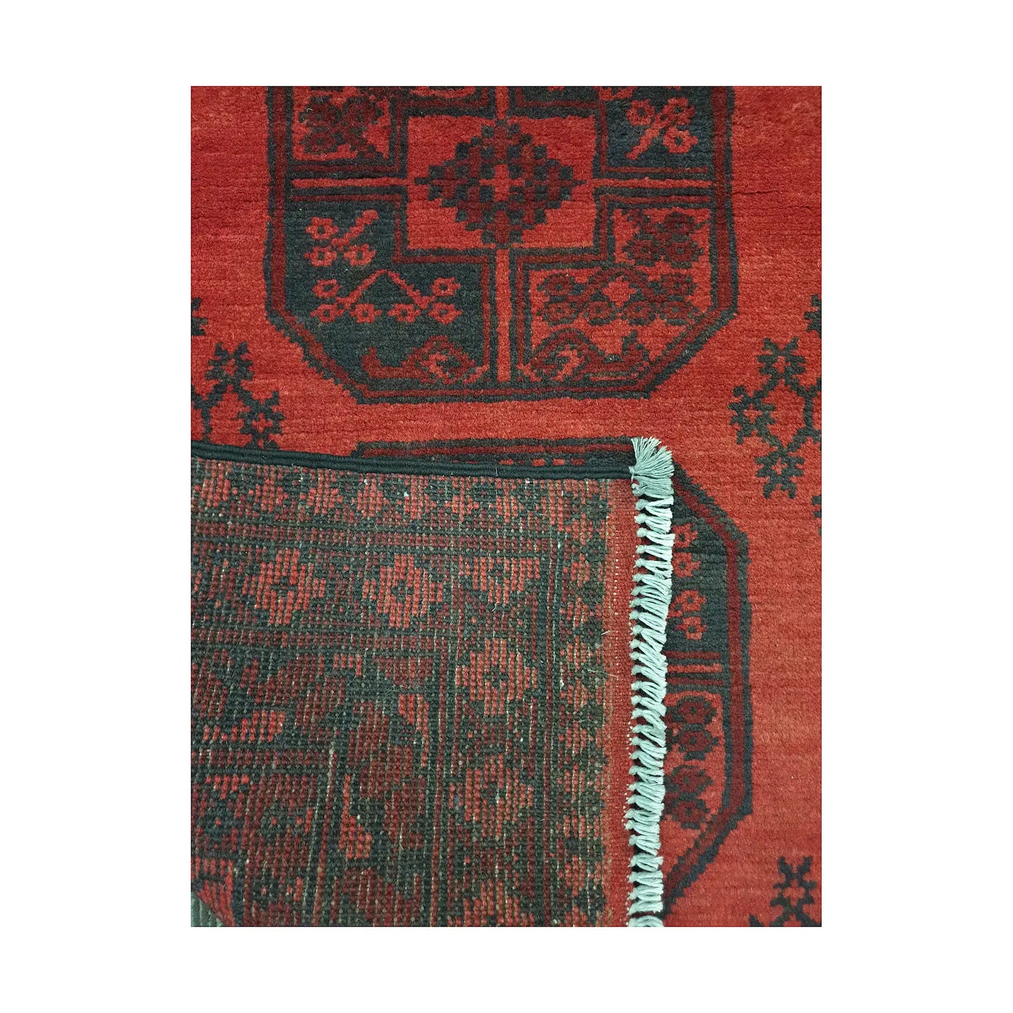 Folded corner detail of Afghan Turkoman rug showing the back of the rug, fringe and red front pattern