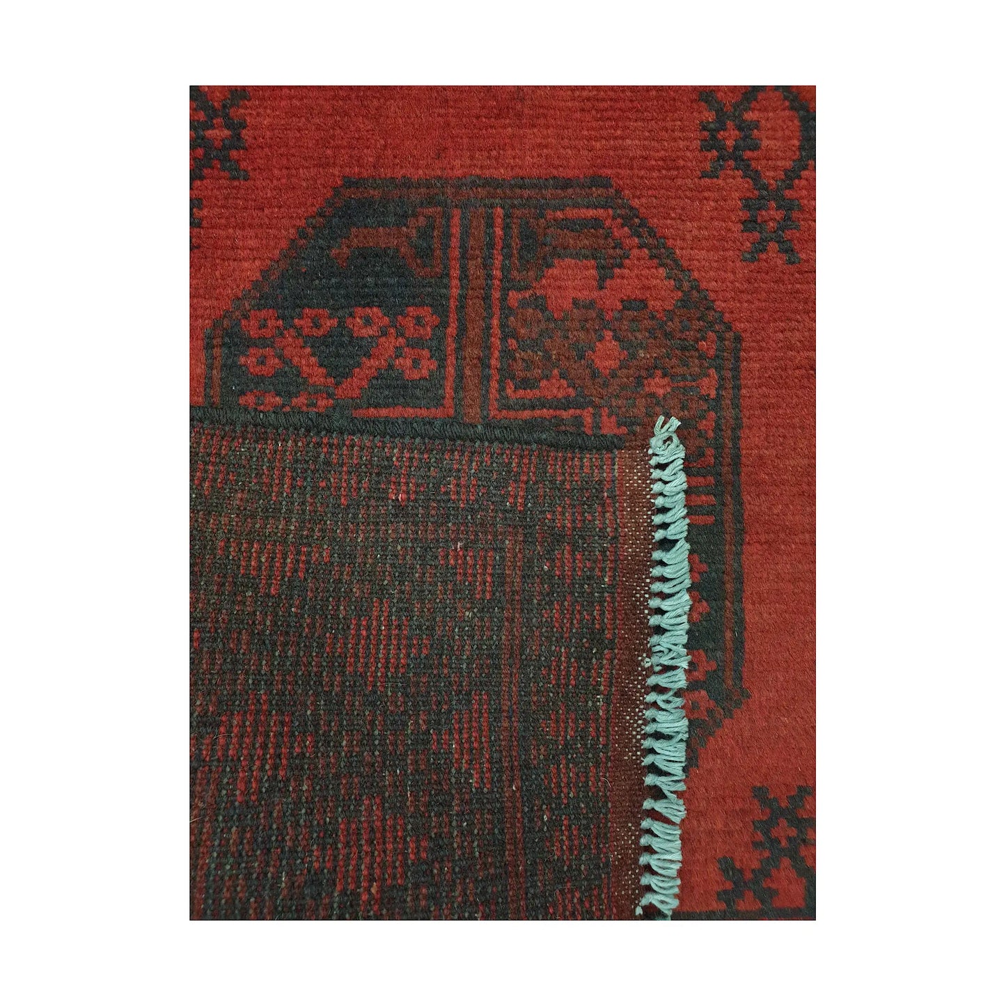 Folded corner detail of Afghan Turkoman rug showing the back of the rug, fringe and red front pattern
