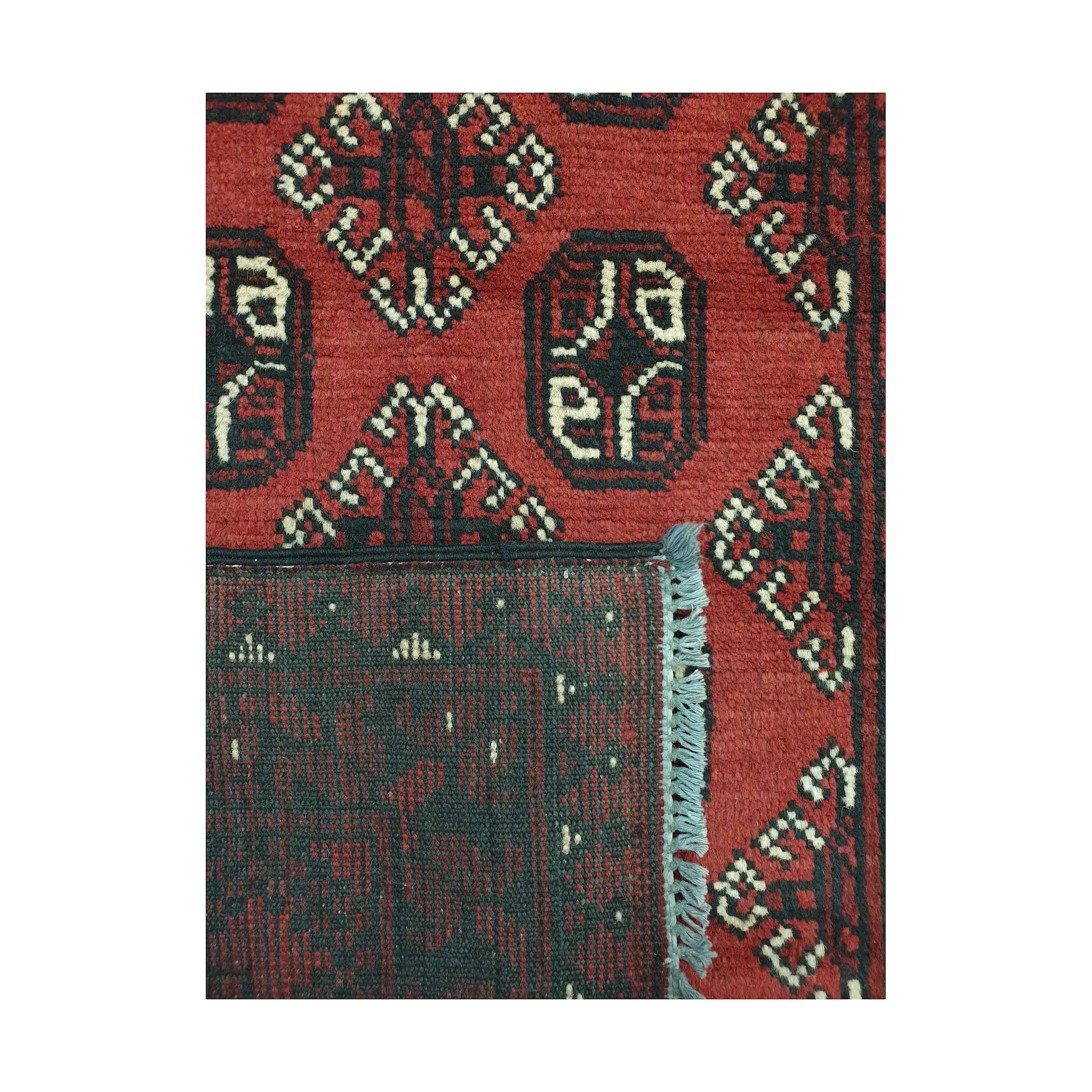Folded corner detail of Afghan Turkoman rug showing the back of the rug, fringe and red front pattern