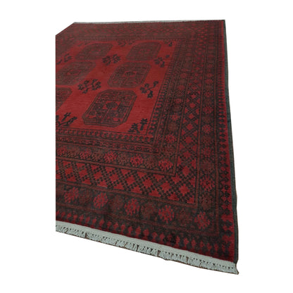 Angled corner detail of Afghan Turkoman wool rug showing the red field, layered geometric borders and visible fringe