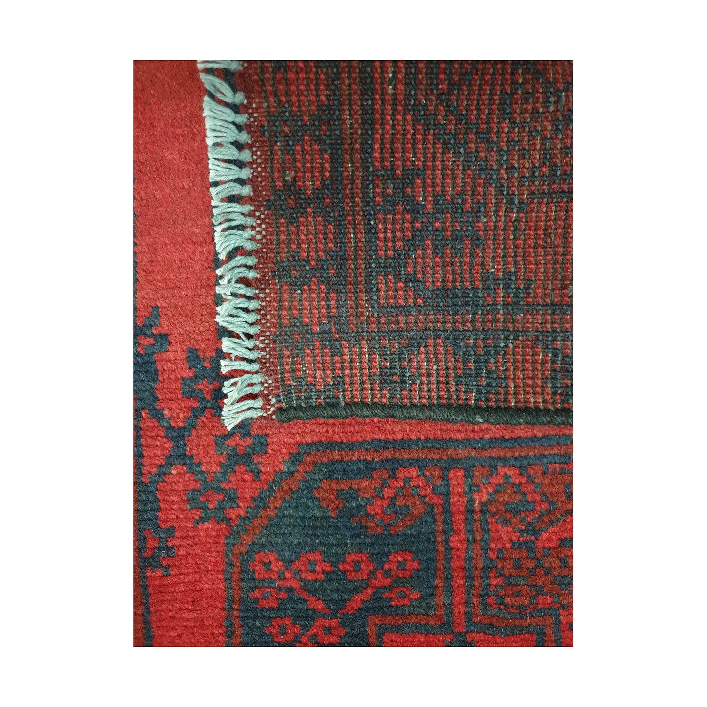 Folded corner detail of Afghan Turkoman runner rug showing the back of the rug, fringe and red front pattern