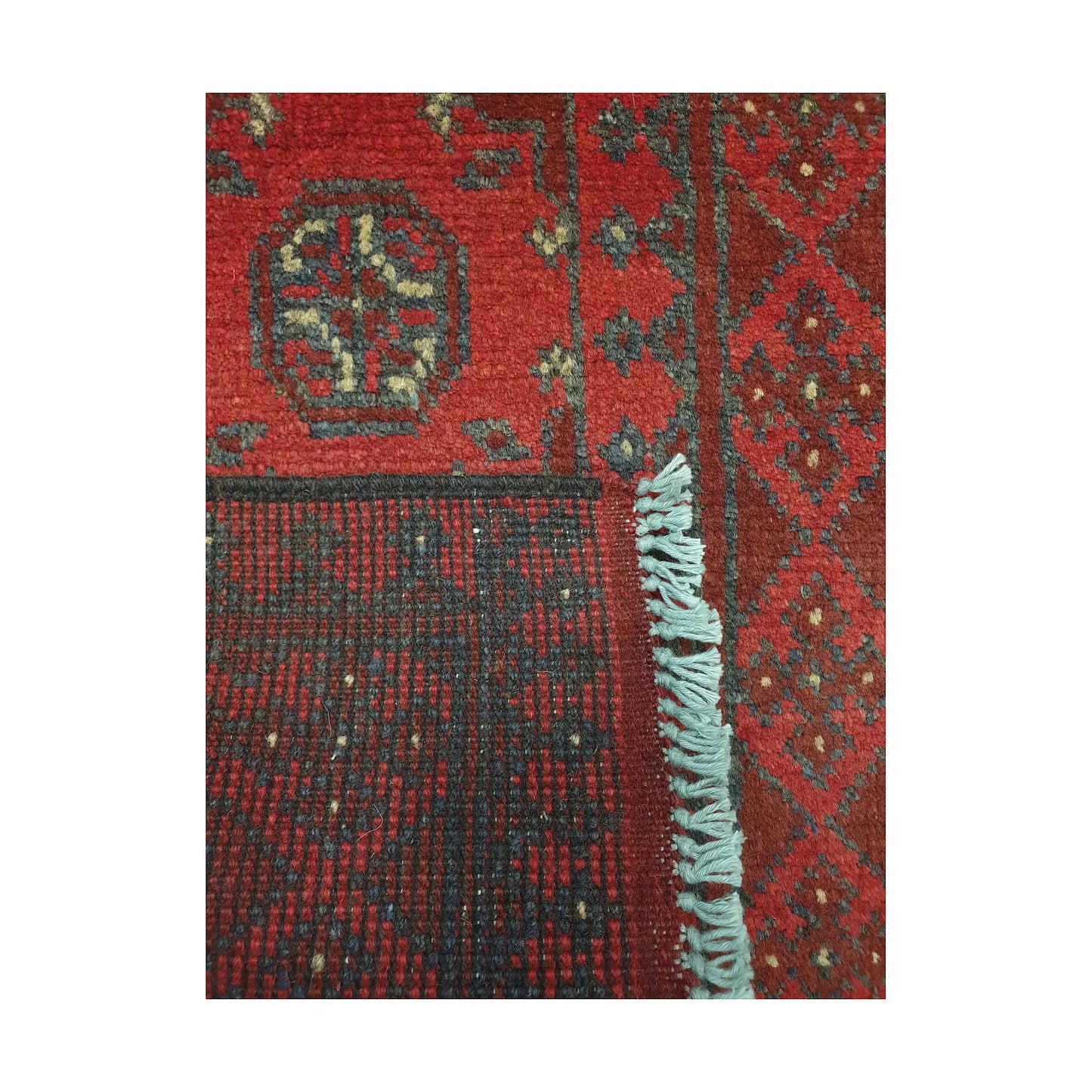 Folded corner detail of Afghan Turkoman runner rug showing the back of the rug, fringe and red front pattern
