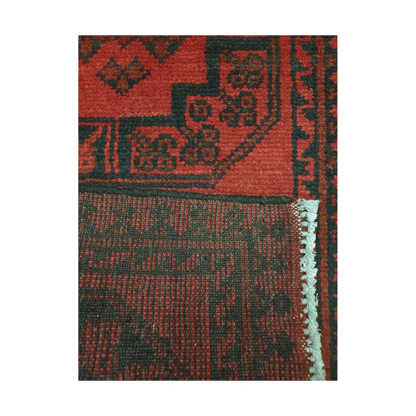 Folded corner detail of Afghan Turkoman runner rug showing the back of the rug, fringe and red front pattern