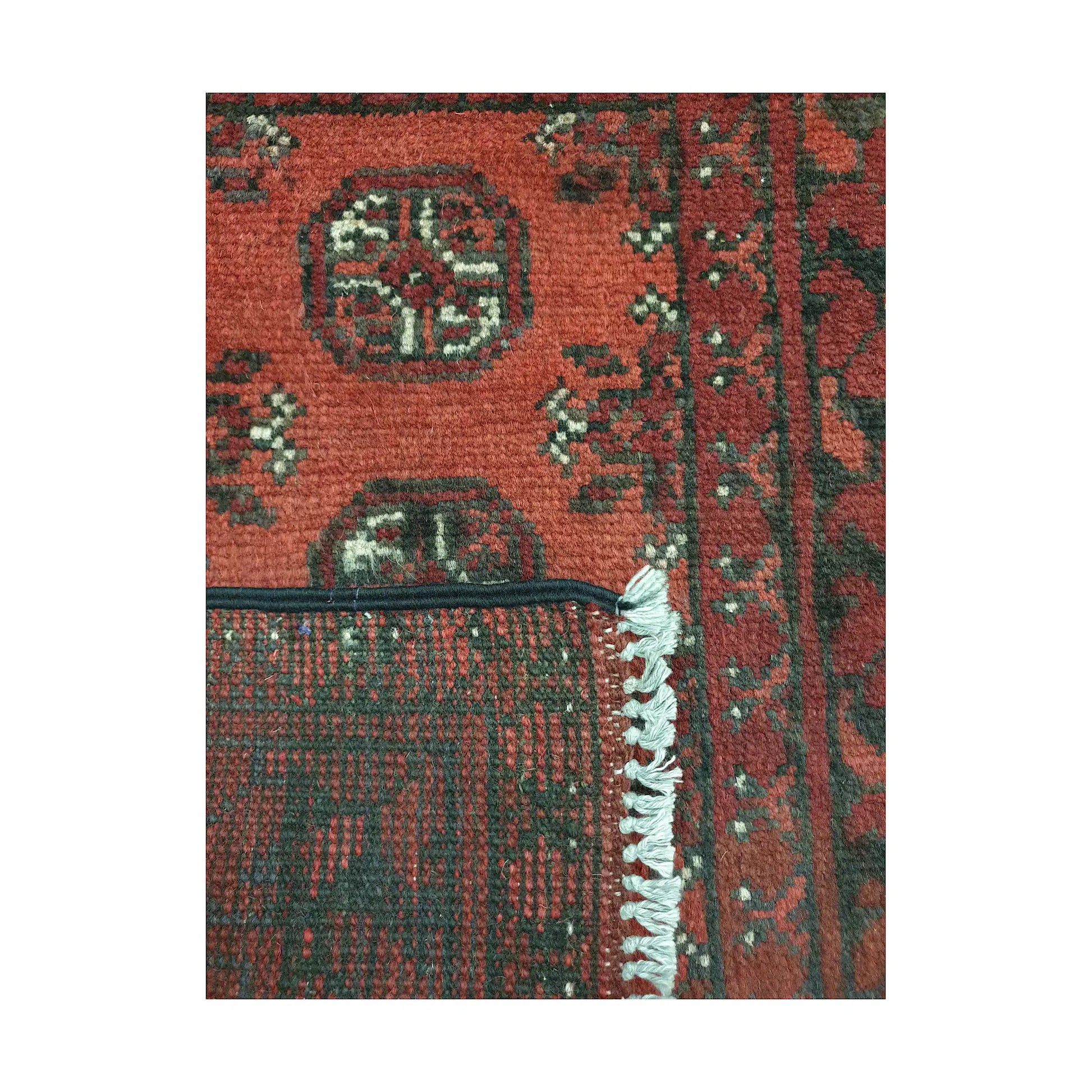 Folded corner detail of Afghan Turkoman wool rug showing the back, fringe and red patterned surface