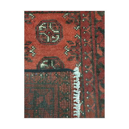 Folded corner detail of Afghan Turkoman wool rug showing the back, fringe and red patterned surface