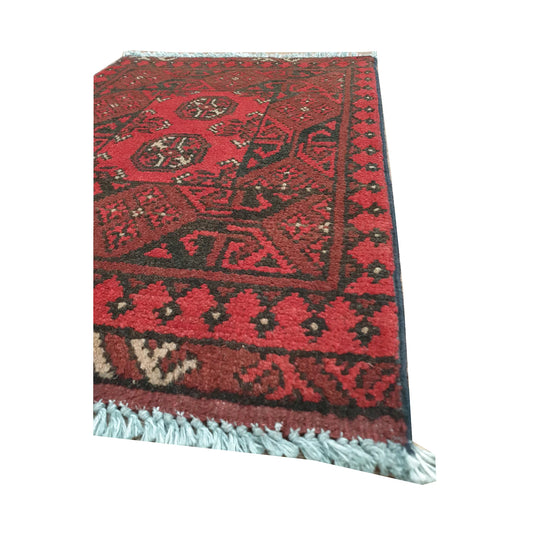 Angled detail of Afghan Turkoman wool rug showing geometric border work and warm red field