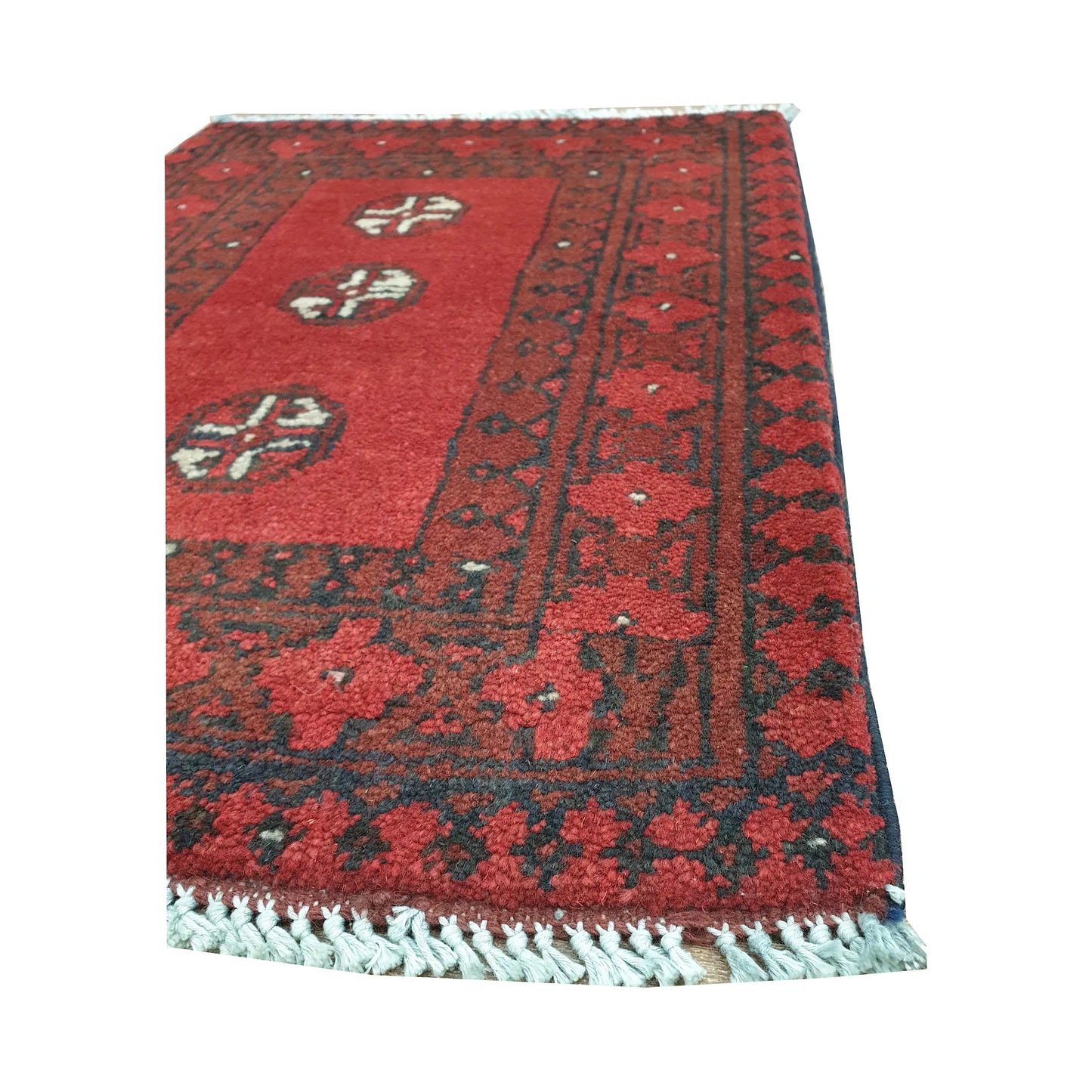 Angled border detail of Afghan Turkoman wool rug showing red floral motifs, dark outlines and fringe