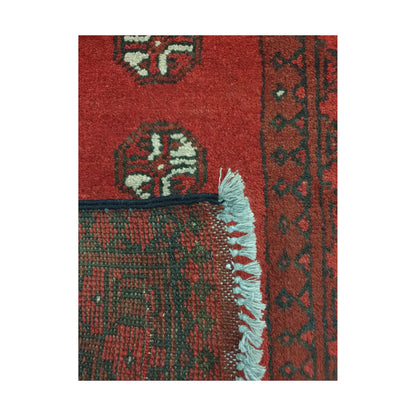 Folded corner detail of Afghan Turkoman wool rug showing the back, fringe and red patterned surface