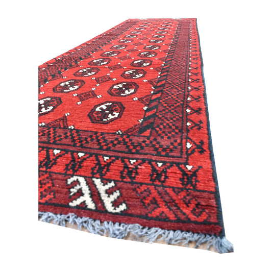 Angled view of Afghan Turkoman wool runner showing oval guls, layered dark borders, ivory end-panel motifs and grey-blue fringe