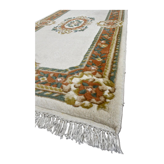 Angled view of Aubusson wool rug showing its ivory field, floral medallion, scrolling border and pale fringe