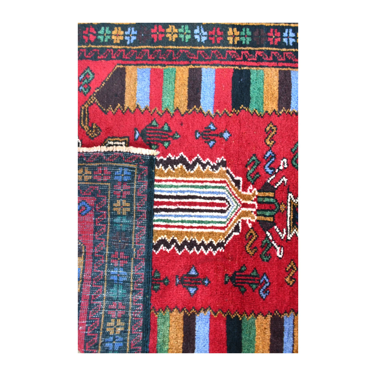 Folded-edge detail of Baluchi rug showing the reverse weave beside its red patterned front and multicoloured stripes