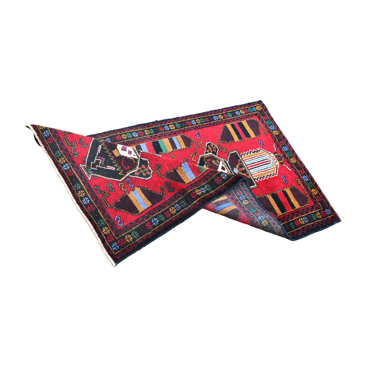 Folded view of Baluchi rug showing its red geometric surface, dark borders and patterned reverse beneath the turned corners