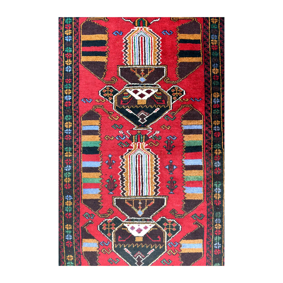 Field detail of Baluchi rug showing two angular medallions, multicoloured striped panels and small motifs across the red ground