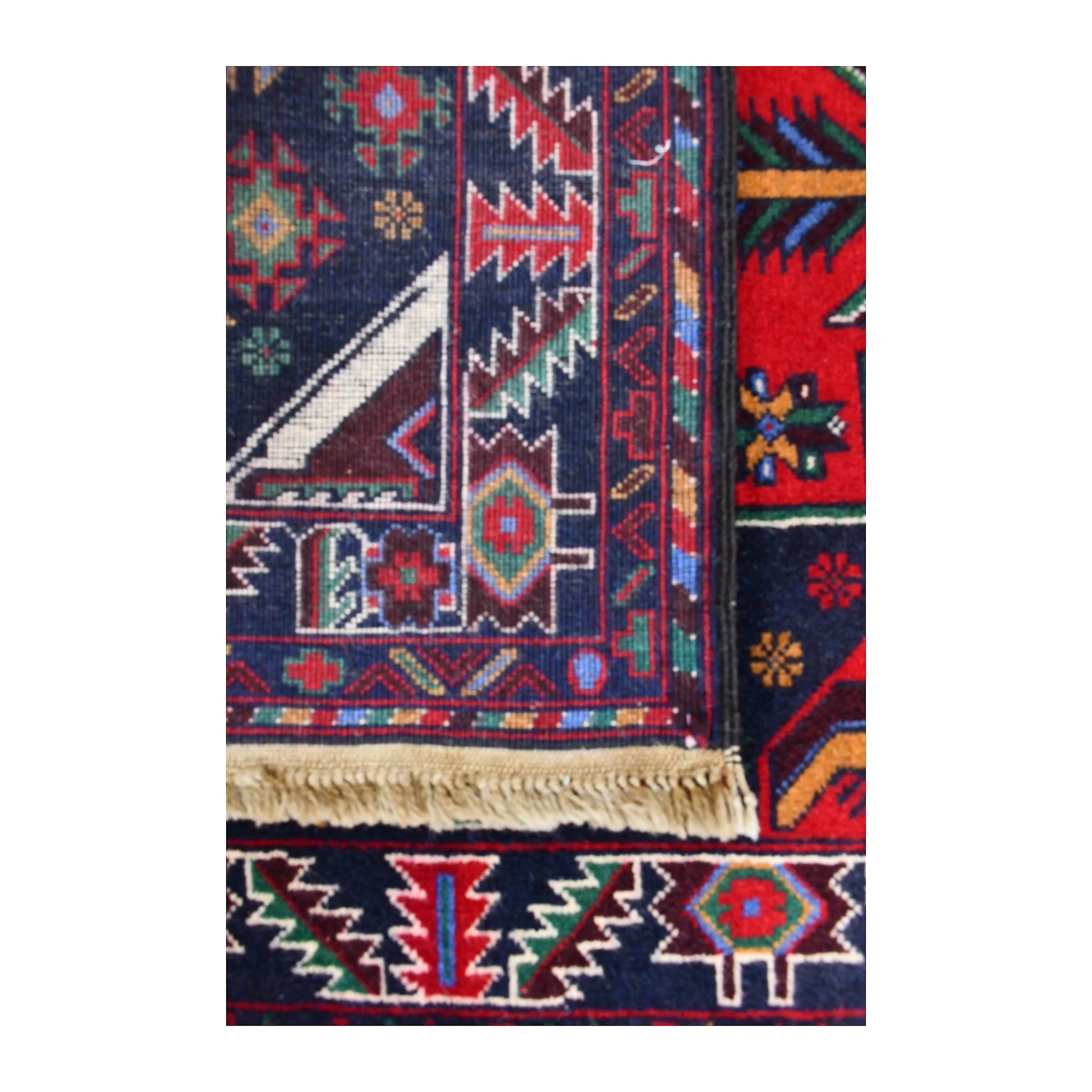 Folded corner of Baluchi runner showing the patterned face, reverse weave and fringed finishing edge