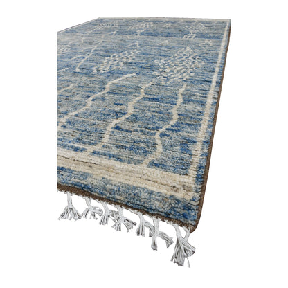 Angled view of the blue Moroccan wool rug showing tonal colour variation, raised ivory motifs and fringe