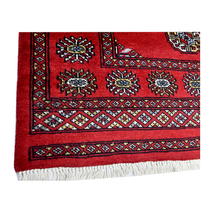 Corner border and fringe detail of Bokhara hand-knotted wool rug showing red field, patterned border and light fringe