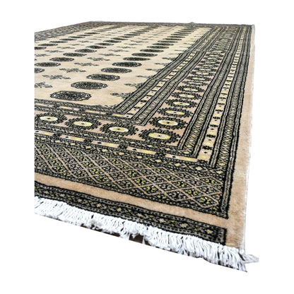 Angled view of Bokhara wool rug showing rows of olive guls across an ivory field, patterned borders and white fringe