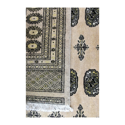 Folded-corner detail of Bokhara rug showing the reverse weave beside its olive, charcoal and ivory patterned front