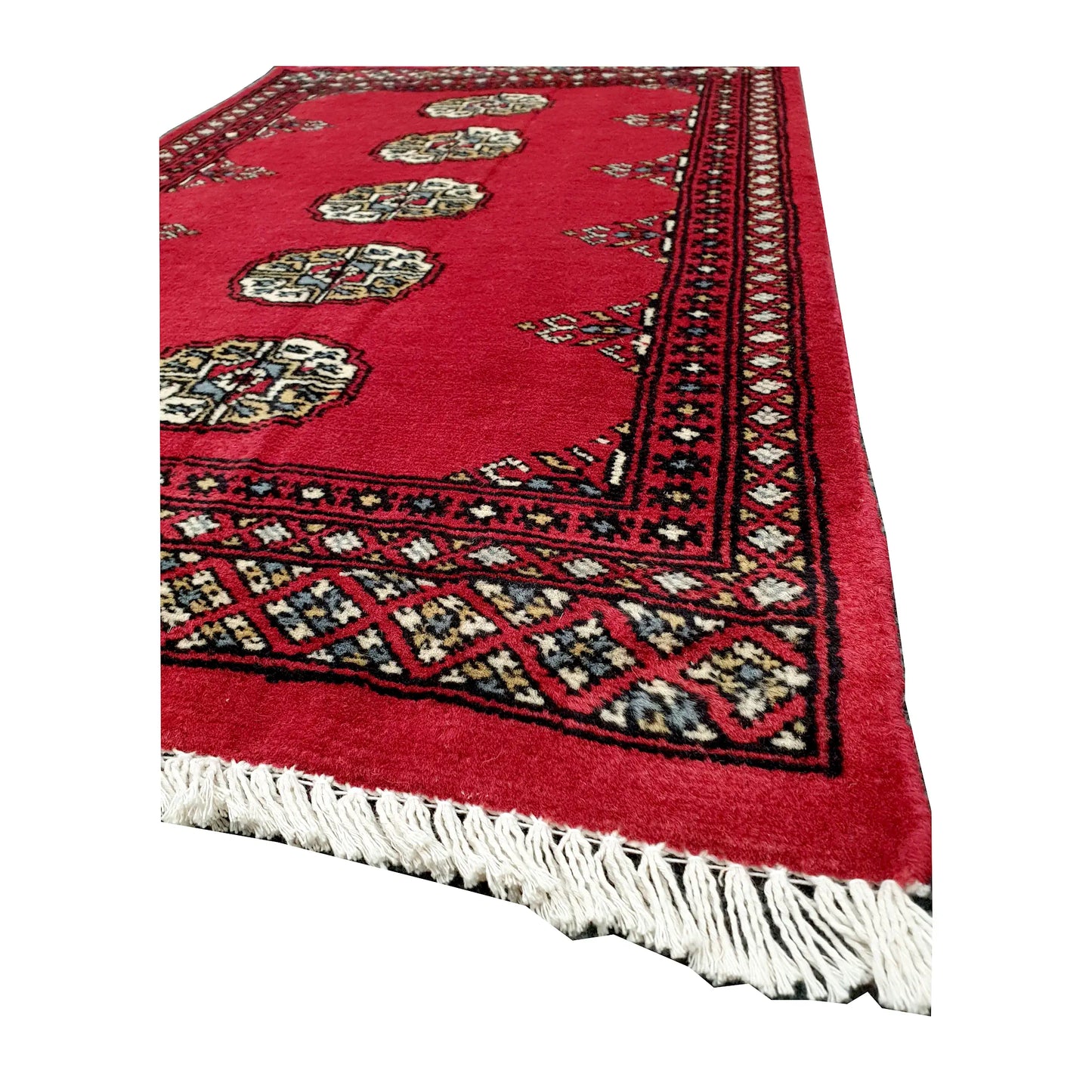 Angled corner and fringe view of Bokhara wool rug showing red field, dark patterned border and light fringe