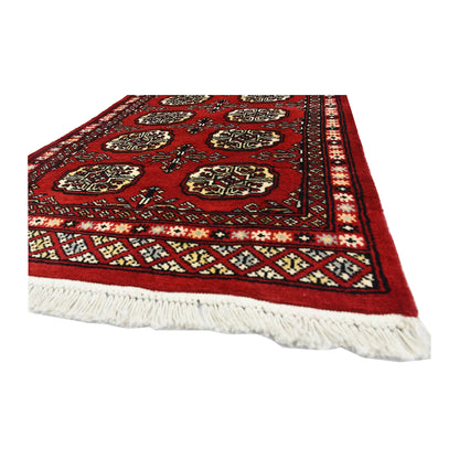 Angled corner and fringe view of Bokhara wool runner rug showing red field, geometric border and ivory fringe