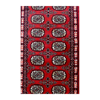 Length field detail of Bokhara wool runner rug showing repeated oval gul-style motifs and geometric border