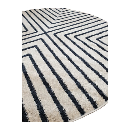Angled view of Primo round rug showing charcoal chevrons across the ivory pile and its bound edge