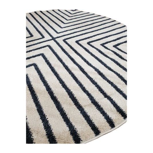 Angled view of Primo round rug showing charcoal chevrons across the ivory pile and its bound edge