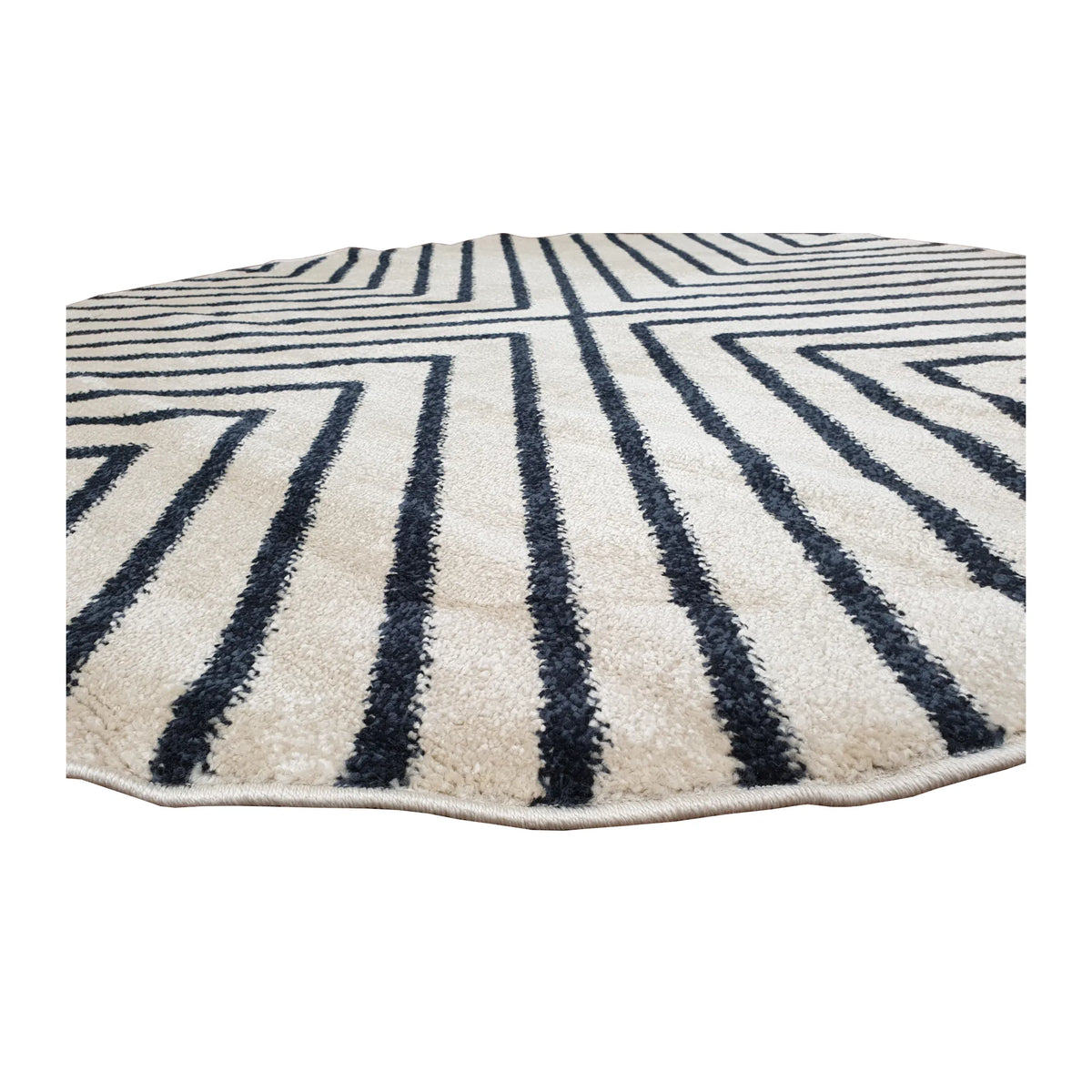 Low-angle close-up of Primo round rug showing textured pile, rounded bound edge and charcoal linear pattern
