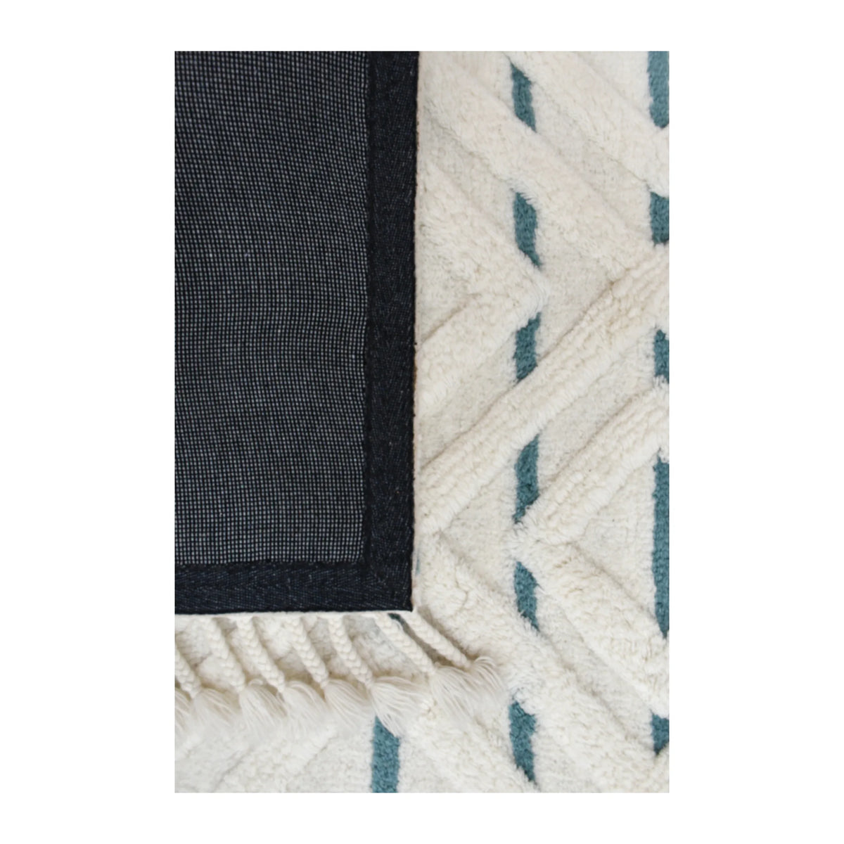 Underside detail of hand-tufted wool rug showing its dark fabric backing beside the cream and blue pile
