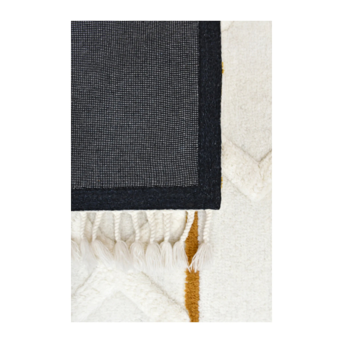 Underside detail of hand-tufted wool rug showing its dark fabric backing beside the cream and mustard pile